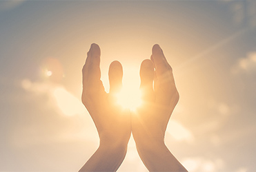 praying hands holding the sun in the sky